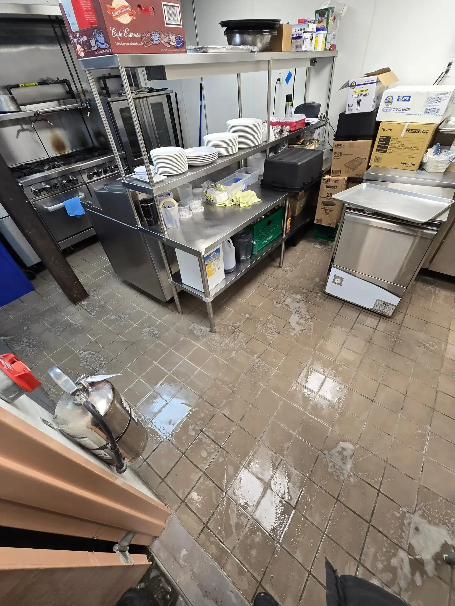 Commercial kitchen tile floor undergoing professional deep cleaning around stainless steel equipment by KG Carpet and Upholstery Cleaning Corp.